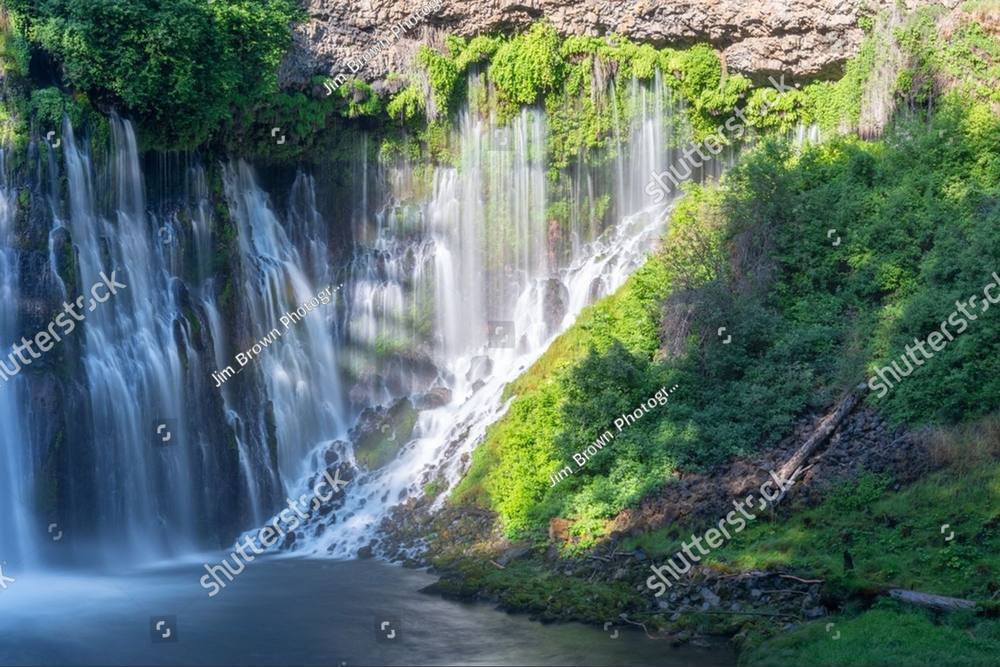 A wide waterfall spilling over a moss-covered green cliff face